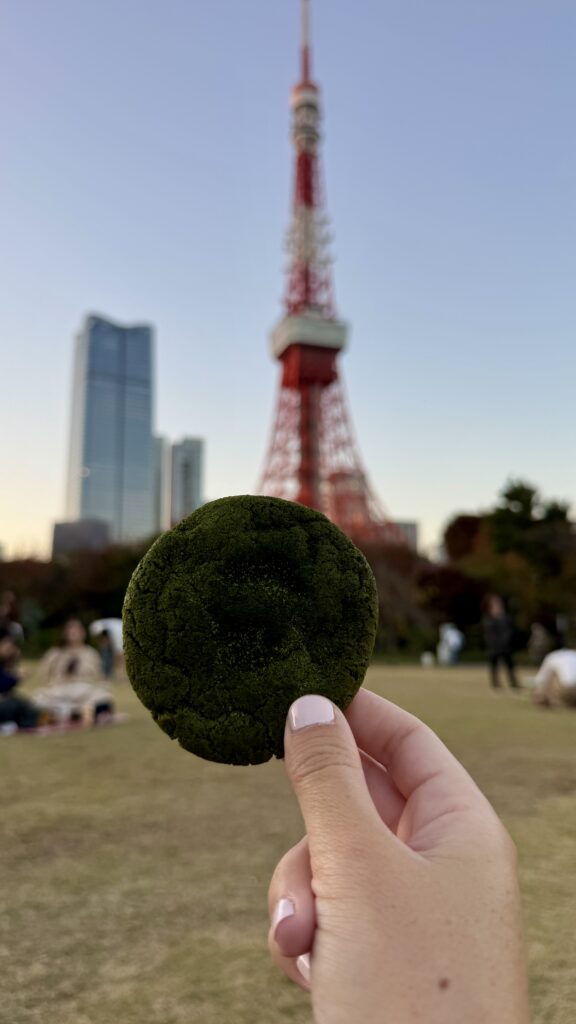 A green matcha cookie from Chavaty Tea and Milk in Omotesando, Tokyo being held in front of the red Tokyo Tower at sunset